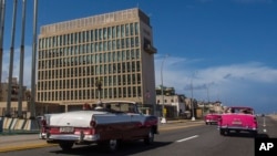 Tourists ride classic cars on the Malecon in Havana, Cuba, Oct. 3, 2017, past the building of the U.S. embassy in the Cuban capital. Efforts are still underway to determine what sickened more than two dozen U.S. diplomats in Cuba since the fall of 2016.