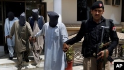 A police officer escorts suspects who allegedly killed Sikh lawmaker Sardar Suran Singh after a press conference in Peshawar, Pakistan, Monday, April 25, 2016.