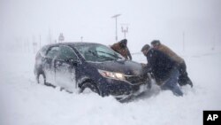 A group of men help a motorist after his vehicle was stuck in the snow near the boardwalk during a snowstorm, Jan. 4, 2018, in Asbury Park, N.J. 