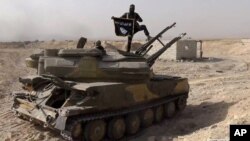 FILE - An Islamic State militant holds the group's flag as he stands on a tank captured from Syrian government forces, in the town of al-Qaryatayn southwest of Palmyra, central Syria.