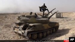 FILE - An Islamic State militant holds the group's flag as he stands on a tank captured from Syrian government forces, in the town of al-Qaryatayn southwest of Palmyra, central Syria. 