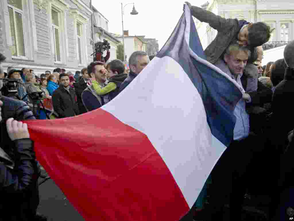 People hold a French flag while waiting to pay their respects to victims of the Paris terrorist attacks, at the French Embassy in Bucharest, Romania, Nov. 15, 2015.