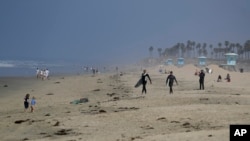 Two surfers walk to the water, May 1, 2020, in Huntington Beach, Calif. California Gov. Gavin Newsom ordered all Orange County beaches closed starting Friday after thousands gathered last weekend in Huntington Beach and Newport Beach.