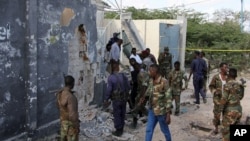 Somali soldiers stand near a destroyed building after a suicide attack that targeted a convoy escorting a senior military general in Mogadishu, Sept, 18, 2016.