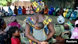 FILE - A mother carrying an infant on her back attends a meeting of women from several communities eradicating female genital mutilation, in Diabougo, Senegal.