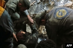FILE - Volunteers of the Syrian Civil Defense, known as the White Helmets, rescue a woman from the rubble of a building after an airstrike in Douma, eastern Ghouta, March 19, 2018.