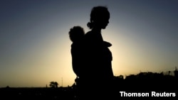 FILE - An Ethiopian woman who fled the ongoing fighting in Tigray region carries her child near the Setit river on the Sudan-Ethiopia border in Hamdayet village in eastern Kassala state, Sudan, Nov. 22, 2020.