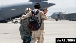 A family walks towards a US Air Force Boeing C-17 Globemaster III during an evacuation at Hamid Karzai International Airport, Afghanistan, Aug. 22, 2021. (US Marine Corps photo)
