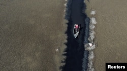ARCHIVO - Isabel Apaza y Gabriel Flores navegan en su bote por un estrecho sendero de agua cerca de la orilla del lago Titicaca en la temporada de sequía en Huarina, Bolivia, el 3 de agosto de 2023.