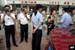 Yuan Shanshan, third right, the wife of detained Chinese lawyer Xie Yanyi, carries her child as she talks to a police officer while other plain clothes security personnel film journalists near the Tianjin No. 2 Intermediate People's Court in northern China's Tianjin Municipality on Tuesday, Aug. 2, 2016.