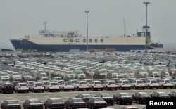 FILE - Newly-manufactured cars and a container ship are seen at Dayaowan port of Dalian, Liaoning province, June 10, 2012.