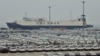 FILE - Newly-manufactured cars and a container ship are seen at Dayaowan port of Dalian, Liaoning province, June 10, 2012. 