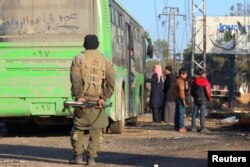 A rebel fighter stands with his weapon near evacuees from the Shi'ite Muslim villages of al-Foua and Kefraya as they ride bueses in insurgent-held al-Rashideen, Syria, Dec. 20, 2016.