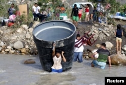 People carry their belongings while crossing the Tachira river border with Venezuela into Colombia, near Villa del Rosario village, Aug. 25, 2015.
