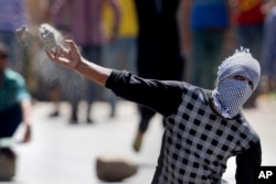 A masked Kashmiri protester throws a rock at policemen in Srinagar, India, Friday, July 8, 2016. Youths in the Indian portion of Kashmir clashed with police during a protest against allegations that Islamic preacher Zakir Naik was involved in making hate speeches.