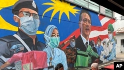 FILE - A Malay couple have lunch next to a graffiti tribute to Malaysian workers on the frontlines against the COVID-19 coronavirus at Damansara in Selangor, outside Kuala Lumpur, Malaysia, Nov. 7, 2020. 