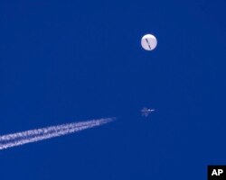 FILE - In this photo provided by Chad Fish, a large balloon drifts above the Atlantic Ocean, just off the coast of South Carolina, with a fighter jet and its contrail seen below it, Saturday, Feb. 4, 2023. The balloon was struck by a missile from an F-22 fighter just off Myrtle Beach, fascinating sky-watchers across a populous area known as the Grand Strand for its miles of beaches that draw retirees and vacationers. (Chad Fish via AP)