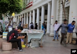 FILE - An Indian man, left, uses his mobile phone as people walk past in New Delhi, India.
