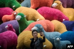 FILE - A woman takes a selfie in front of a multi-colored sheep installation displayed in a shopping mall for the Chinese New Year celebrations in Hong Kong, Feb. 18, 2015.