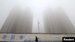 A woman wearing a mask walks past buildings on a polluted day in Handan, Hebei province, China, Jan. 12, 2019. China is reportedly the world's top emitter of greenhouse gases.