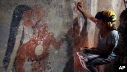 Conservator Angelyn Bass cleans and stabilizes the surface of a wall of a Maya house that dates to the 9th century A.D. The figure of a man who may have been the town scribe appears on the wall to her left. (Tyrone Turner © 2012 National Geographic)