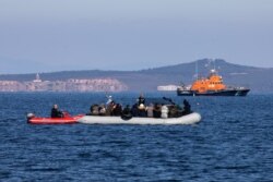 FILE - Migrants on a dinghy are approached by a Greek coast guard boat near the port of Thermi, as they crossed part of the Aegean Sea from Turkey to the island of Lesbos, Greece, March 1, 2020.