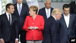 File - French President Emmanuel Macron, left, speaks with German Chancellor Angela Merkel, second left, as President Trump takes his position during a group photo at the new NATO headquarters in Brussels on Thursday, May 25, 2017. 