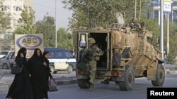 FILE - Afghan women walk as a British soldier arrives at the site of a blast in Kabul, Afghanistan, Aug. 22, 2015.