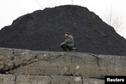 FILE - A North Korean man sits beside a pile of coal on the bank of the Yalu River in the North Korean town of Sinuiju.