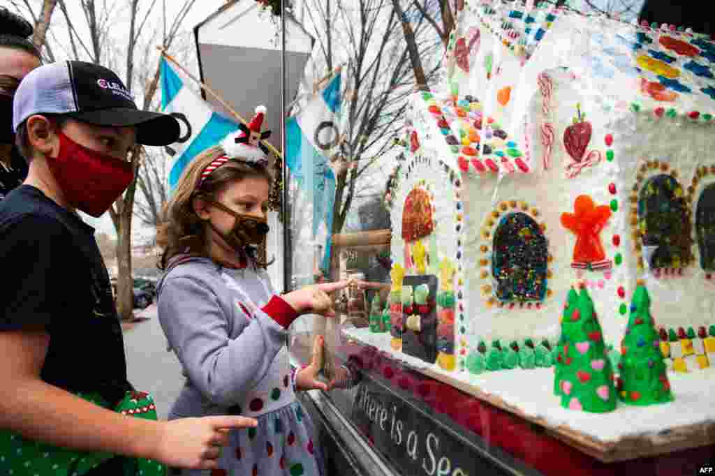 Dos niños disfrutan viendo las decoraciones navideñas, incluida una casa de pan de jengibre gigante, en los escaparates de la tienda Country en Main Street en Stockbridge, Massachusetts, el 13 de diciembre de 2020. [AFP] 