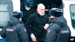 A man is being escorted out of a police van after he was detained in Moscow, Russia, March 13, 2021. 
