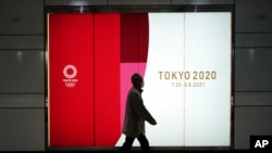 FILE - A man wearing a mask to protect against the coronavirus walks past a banner advertising the postponed Tokyo 2020 Olympics, in an underpass in Tokyo, Japan, Jan. 19, 2021. 