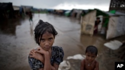 In this June 26, 2014 photo, a girl, self-identified as Rohingya, stands close to her family's tent house at Dar Paing camp for refugees, suburbs of Sittwe, Western Rakhine state, Myanmar.