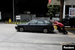 Attendants push a car at a gas station of Venezuelan state-owned oil company PDVSA in Caracas, Venezuela, Sept. 21, 2017.