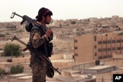 This April 30, 2017, photo provided by the Syrian Democratic Forces (SDF) shows a fighter from the SDF carrying weapons as he looks toward the northern town of Tabqa, Syria.