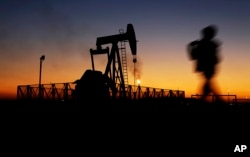 A boy walks by an oil pump at sunset Jan. 18, 2016, in the desert oil fields of Sakhir, Bahrain.