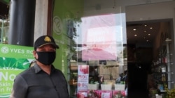 Security guard Noep Boeun has two jobs: watching the entrance of a cosmetic shop for potential theft and checking customers' temperature for fever, Phnom Penh, Cambodia, March 27, 2020. (Phorn Bopha/VOA Khmer).