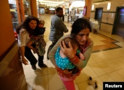Women carrying children run for safety as armed police hunt gunmen who went on a shooting spree in Westgate shopping center in Nairobi, Sept. 21, 2013.