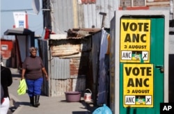 A woman, left, passes a poster for African National Congress, ANC, in Khayelitsha township outside Cape Town, South Africa, Aug. 1, 2016. South Africa's ruling party faces a significant challenge in Wednesday's municipal elections.