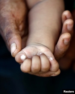 A Rohingya refugee woman holds the hand of her 3-month-old daughter after crossing the Bangladesh-Myanmar border while being detained by the Border Guard Bangladesh (BGB) near Inani beach in Cox's Bazar, Bangladesh, Nov. 7, 2017.