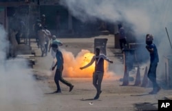 FILE - A tear gas shell fired by an Indian policeman explodes behind Kashmiri protesters during a protest in Srinagar, Indian controlled Kashmir, June 16, 2017.