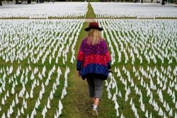 FILE - Artist Suzanne Brennan Firstenberg walks among thousands of white flags planted in remembrance of Americans who have died of COVID-19 near Robert F. Kennedy Memorial Stadium in Washington.