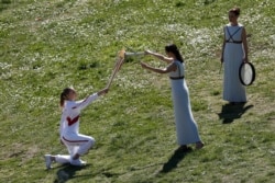 Greek actress Xanthi Georgiou, center, lights the torch of the 2020 Tokyo Olympic Games, held by Greek shooting Olympic champion Anna Korakaki, left, during the flame lighting ceremony at the closed Ancient Olympia site in southern Greece.