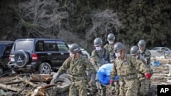 Members of the Japan Self-Defense Force carry the body of a victim found amid the rubble in Noribu, northern Japan, as pressure mounts to expand an evacuation zone around the crippled nuclear plant where radioactive iodine was detected in the groundwater 