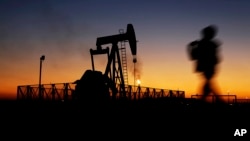 Seorang anak laki-laki berjalan melintasi sebuah pompa angguk minyak saat matahari terbenam di lapangan minyak Sakhir, Bahrain, 18 Januari 2016. 
