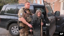 In this photo provided by Ukrainian National Police of Donetsk region, Lidia Lomikovska, 98, is helped by a police officer after she escaped Russian-occupied territory, April 26, 2024. Lomikovska left her frontline town of Ocheretyne by walking almost 10 km (6 miles) alone.