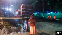 Seorang anggota kepolisian Thailand berjaga di bawah hujan dekat gua Tham Luang di Taman Hutan Khun Nam Nang Non di distrik Mae Sai, provinsi Chiang Rai, tanggal 7 Juli 2018 (foto: AFP Photo/Ye Aung Thu)