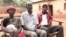 Silas Bihizi, center, sits with Valens Rukiriza, right, Rukiriza's wife and one of their grandchildren outside the Rukiriza family home in Buguli, Rwanda. 