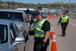 FILE - New Mexico state police officers screen cars for compliance with an emergency lockdown order that bans nonessential visitors and limits vehicle passengers to two people as they enter Gallup, N.M., May 7, 2020.