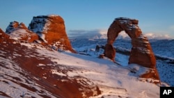 FILE - Delicate Arch glows in light from the setting sun as alpenglow lights up the La Sal mountains in the distance, Dec. 31, 2010 at Arches National Park near Moab, Utah.